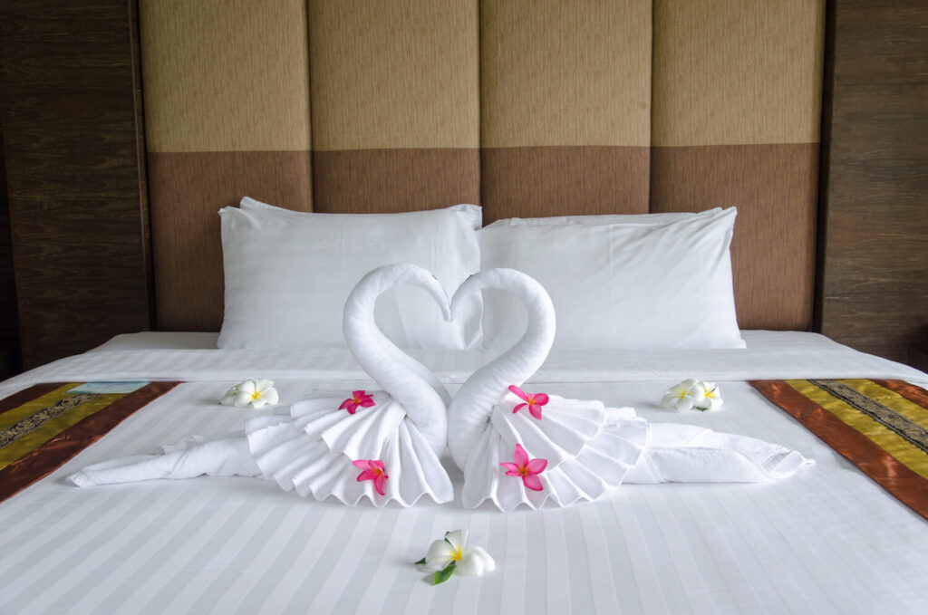 Two towel swans with flowers on a bed