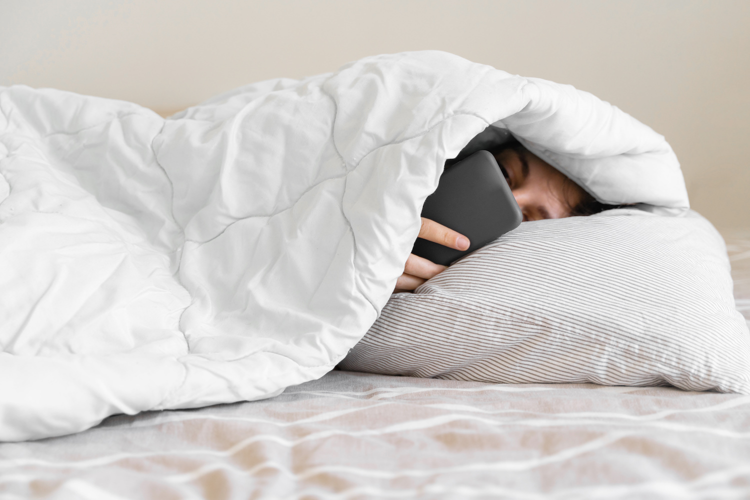 Woman under the bed covers with her phone