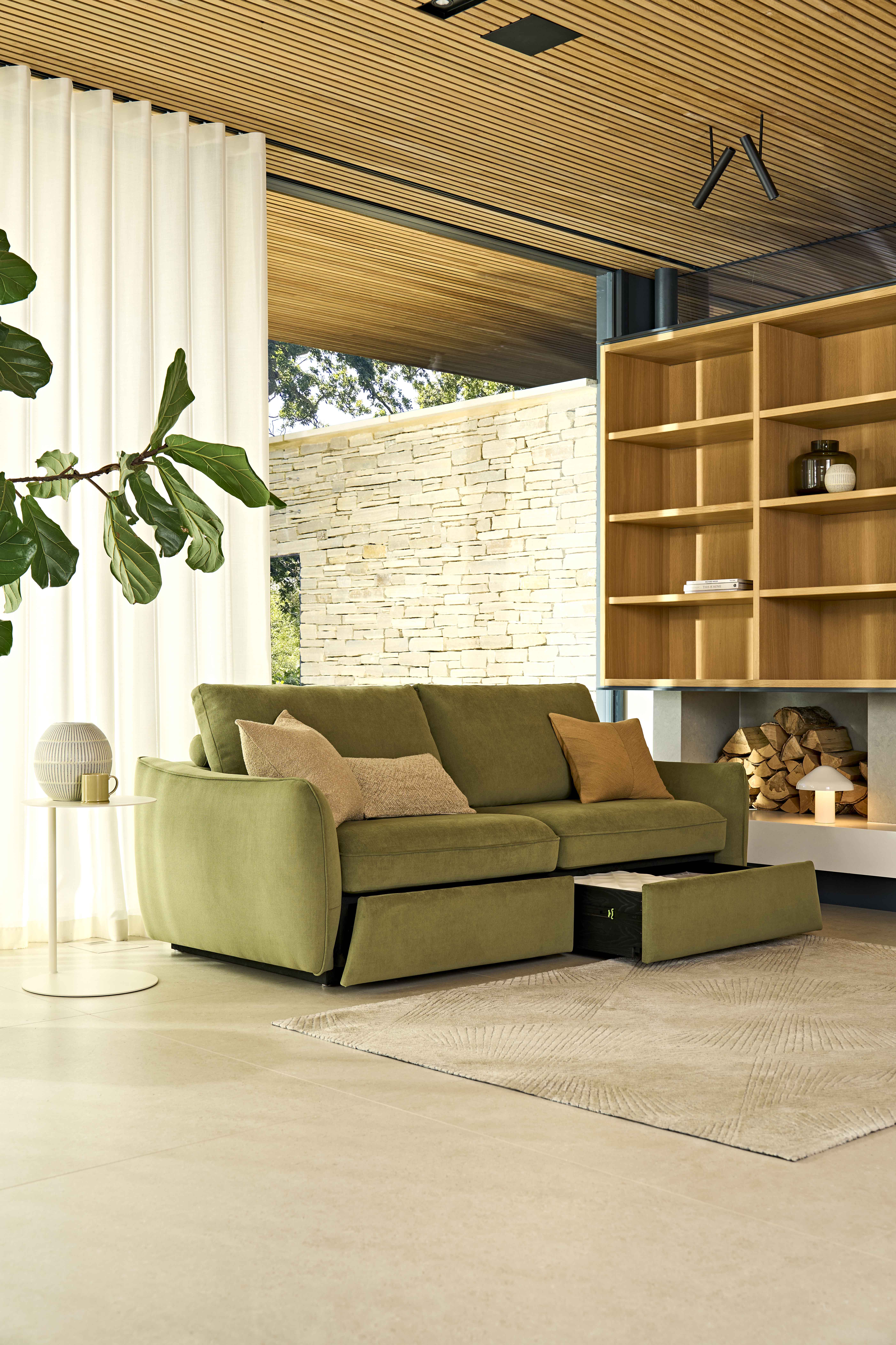 The Mellow storage sofa in olive green, sitting in a calm modern living room with wooden ceiling and bookshelves